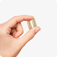 Conceive Plus Max Couples Fertility Bundle featuring two beige women’s ovulation support capsules held gently between fingers, highlighting smooth surface and natural tone, captured on a white background.