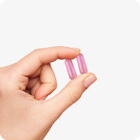 Conceive Plus Max Couples Fertility Bundle featuring pink women's fertility support capsules held delicately between fingers, highlighting capsule color, size, and texture against a white background.