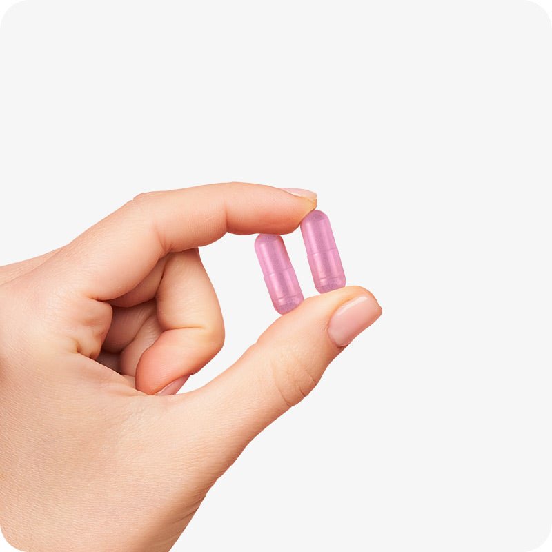 Conceive Plus Max Couples Fertility Bundle featuring pink women's fertility support capsules held delicately between fingers, highlighting capsule color, size, and texture against a white background.
