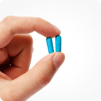 Conceive Plus Max Couples Fertility Bundle close-up of two blue men's fertility support capsules held gently between fingers, highlighting capsule size and texture on a bright white background.