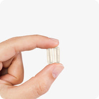 Conceive Plus Max Couples Fertility Bundle featuring two beige men's motility support capsules held between fingers, highlighting capsule clarity, size, and smooth texture on a white background.