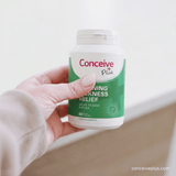 Hand holding a bottle of Conceive Plus morning sickness relief supplement against a light background